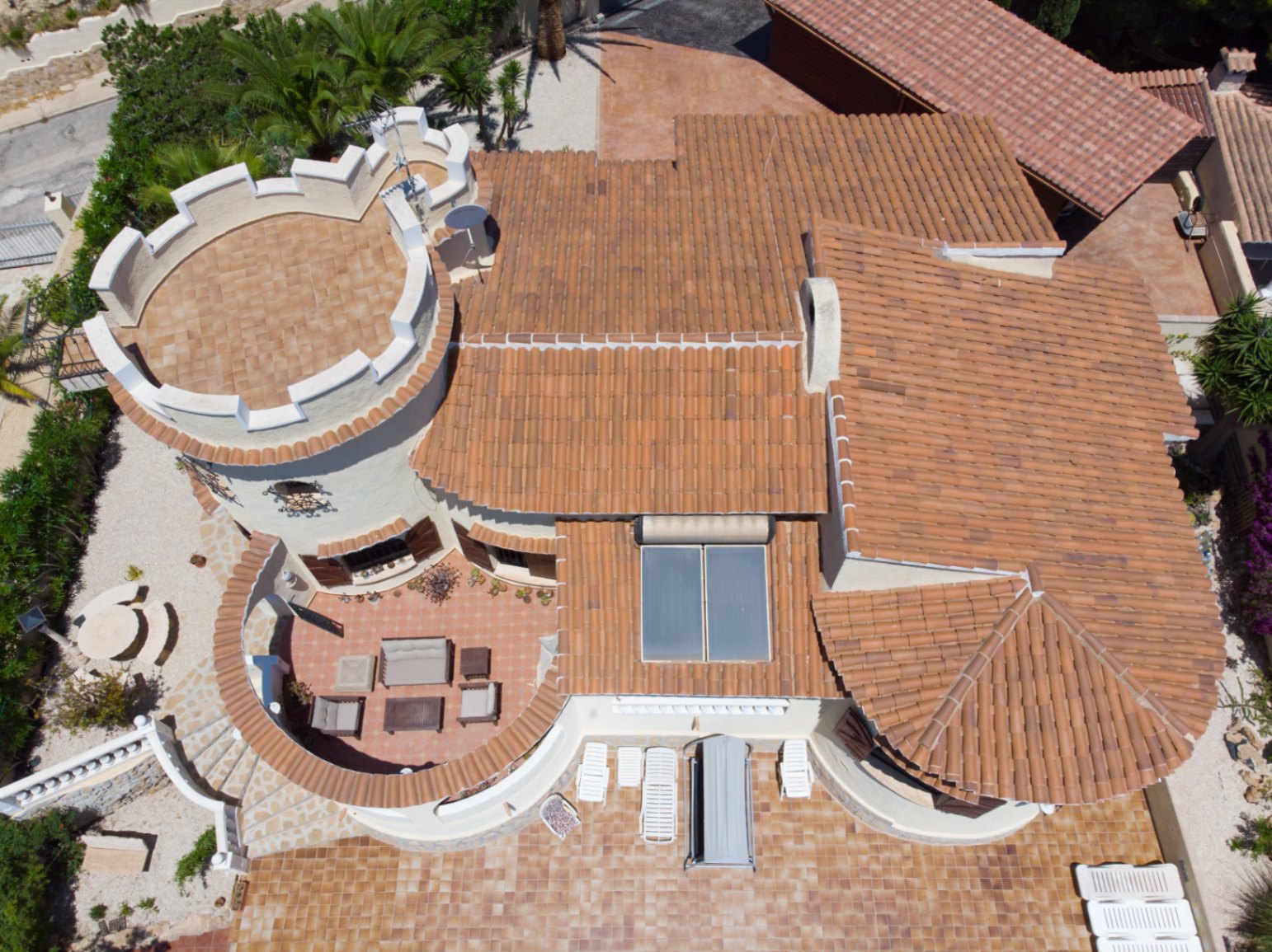 Luftaufnahme der Villa mit dem markanten Zinnenturm, den Terrakotta-Ziegeldächern mit Sonnenkollektoren und den großzügigen, möblierten Außenterrassen.