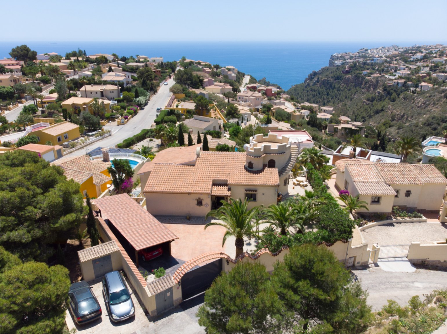 Luftaufnahme der Villa mit ihrem markanten Turm, dem Carport und dem angelegten Grundstück mit Panoramablick auf das Mittelmeer.