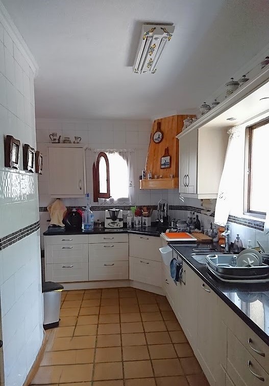 Separate Küche mit weißen Schränken, dunklen Arbeitsplatten und Terrakottaboden. Ausgestattet mit einer Dunstabzugshaube aus Holz und natürlichem Lichteinfall.