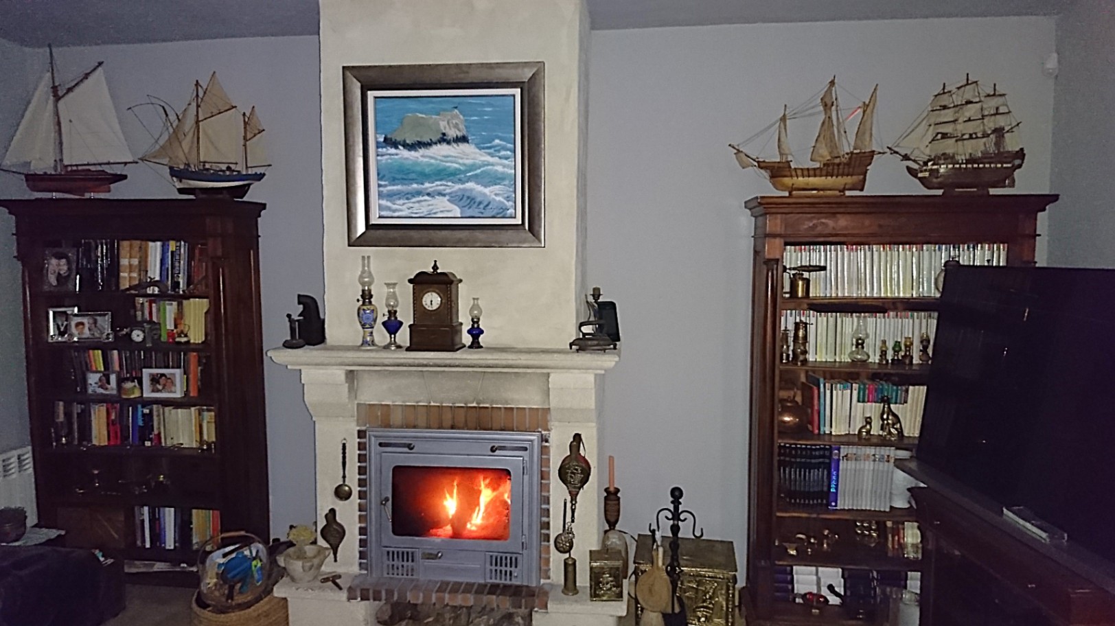 Traditioneller Wohnbereich mit gemauertem Kamin und Kassetteneinsatz, flankiert von klassischen Holzregalen mit maritimer Dekoration und Schiffsmodellen.