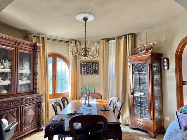 Traditionelles Esszimmer mit massiven Holzvitrinen, einem klassischen Kronleuchter und einem markanten Rundbogenfenster mit Holzrahmen.