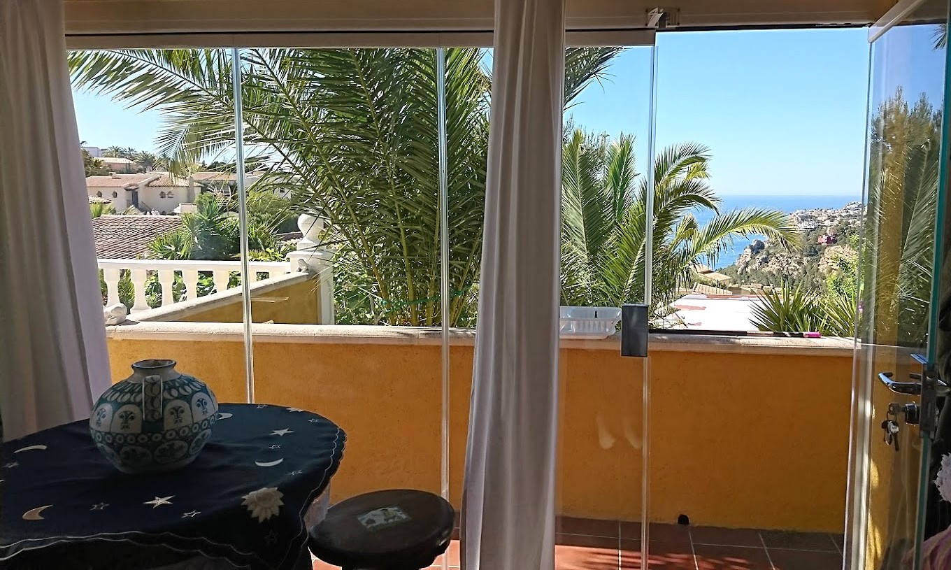 Verglaste Terrasse mit faltbaren Glassystemen, Terrakottaboden und Panoramablick auf das Mittelmeer zwischen Palmen.