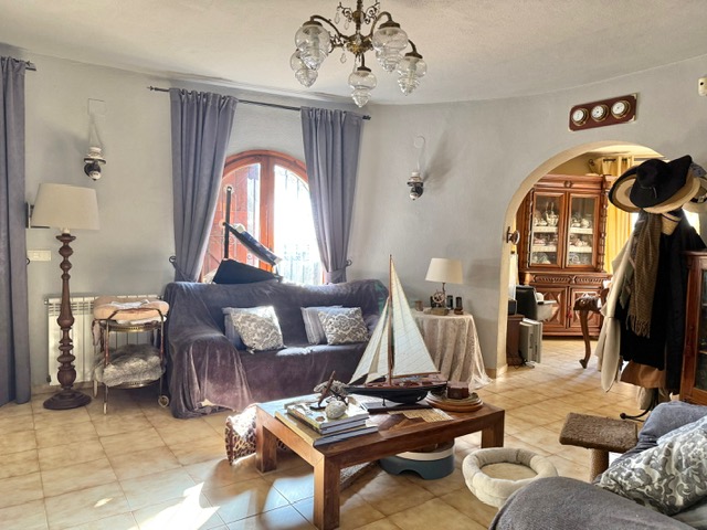 Wohnzimmer mit geschwungenen Wänden, Fliesenboden und Rundbogen zum Esszimmer. Ausgestattet mit einem Holz-Bogenfenster, Kronleuchter und Zentralheizung.