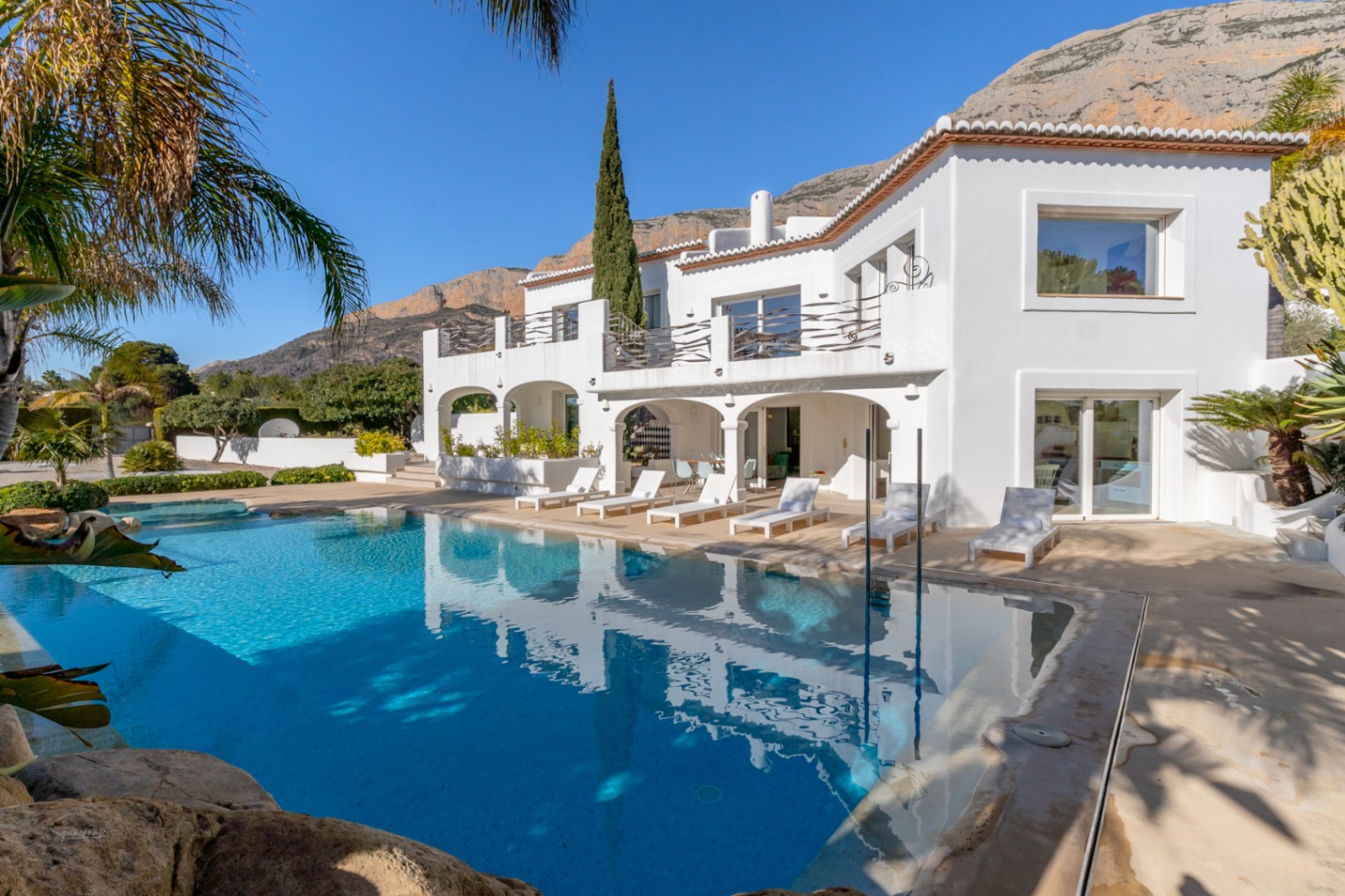 Außenansicht der Villa im Ibiza-Stil mit 70 m² Pool, bogenförmiger Naya und Terrasse vor der Kulisse des Montgó-Massivs.