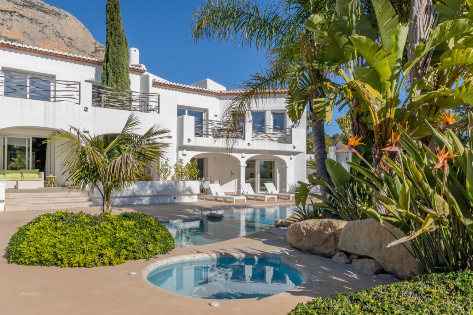 Außenansicht der Villa im Ibiza-Stil mit Designer-Pool, integriertem Whirlpool und Rundbogennaya vor der Kulisse des Montgó-Massivs und Palmen.