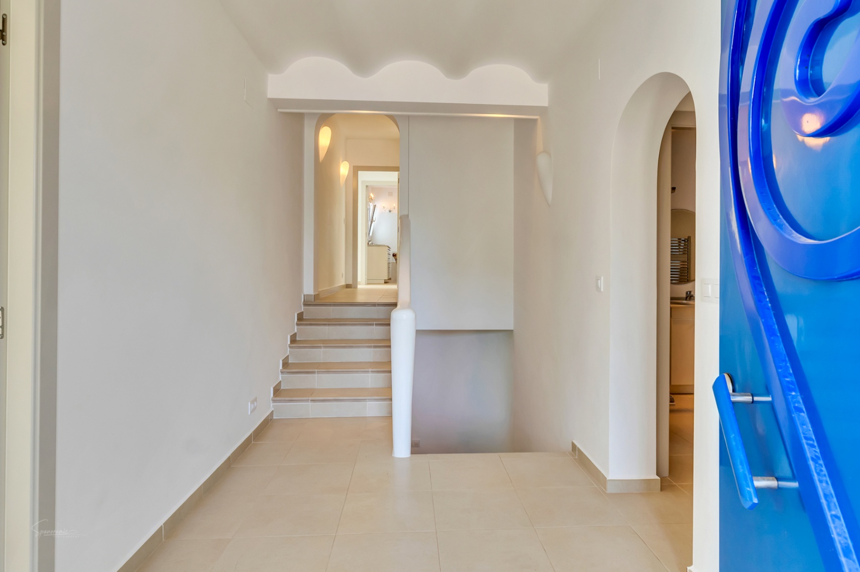 Eingangsbereich mit markanter blauer Designtür, wellenförmigen Deckenverzierungen und Treppenzugängen zu beiden Ebenen der Villa.