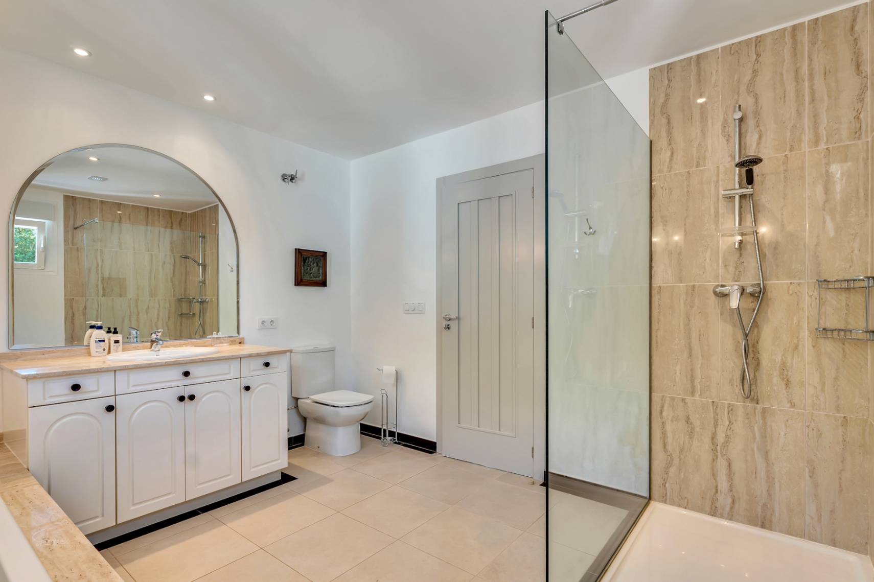 Elegantes Badezimmer mit begehbarer Dusche aus Naturstein, weißem Waschtisch mit Marmorplatte und einem großen Rundbogenspiegel mit Einbaustrahlern.