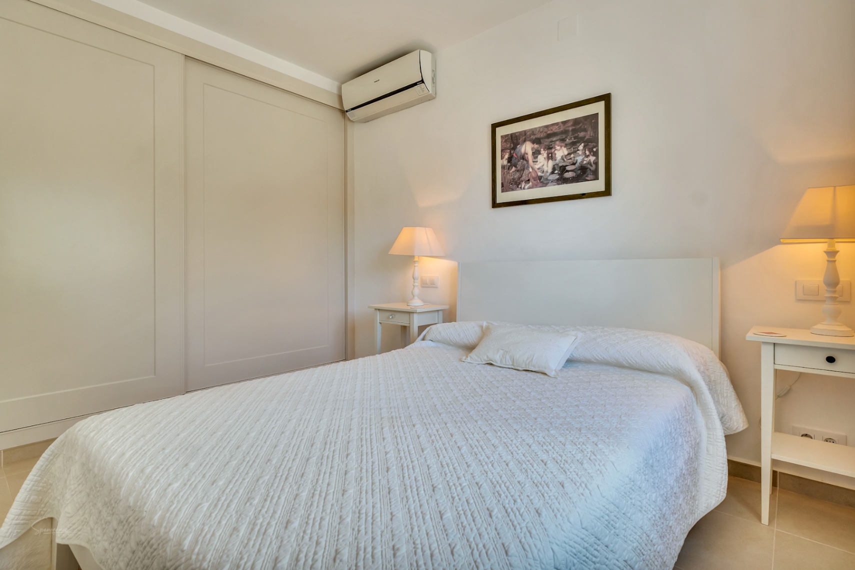 Hell gestaltetes Schlafzimmer mit großem Einbauschrank, Split-Klimaanlage und passenden Nachttischen in einer warmen, einladenden Atmosphäre.