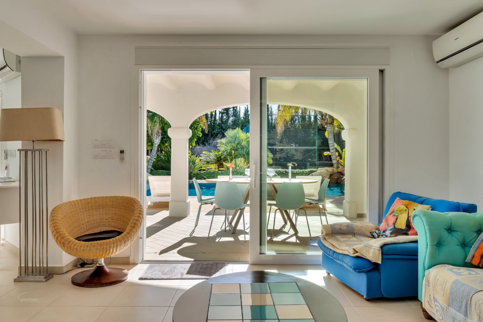Heller Wohnbereich mit Glasschiebetür zur überdachten Naya mit weißen Rundbögen, Blick auf den privaten Pool und den mediterranen Garten.