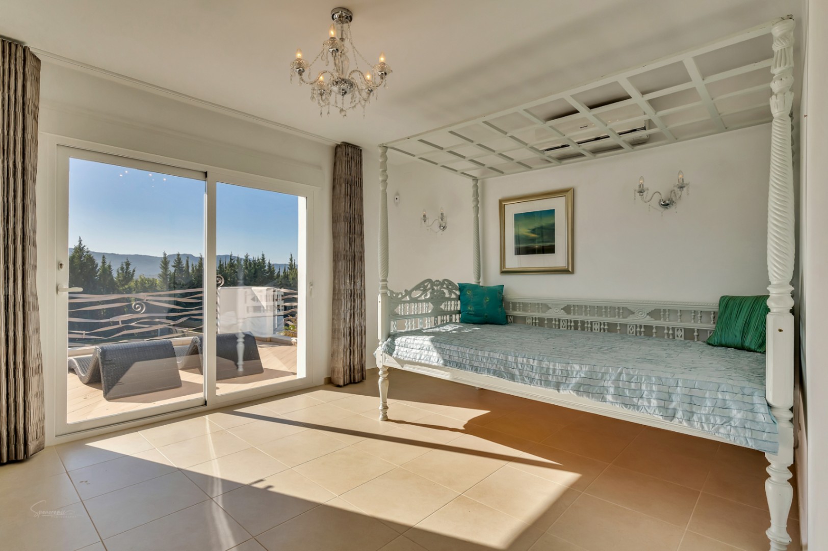Helles Schlafzimmer mit einem kunstvoll geschnitzten weißen Himmelbett und direktem Zugang zur sonnigen Terrasse mit weitem Blick auf die Berglandschaft.