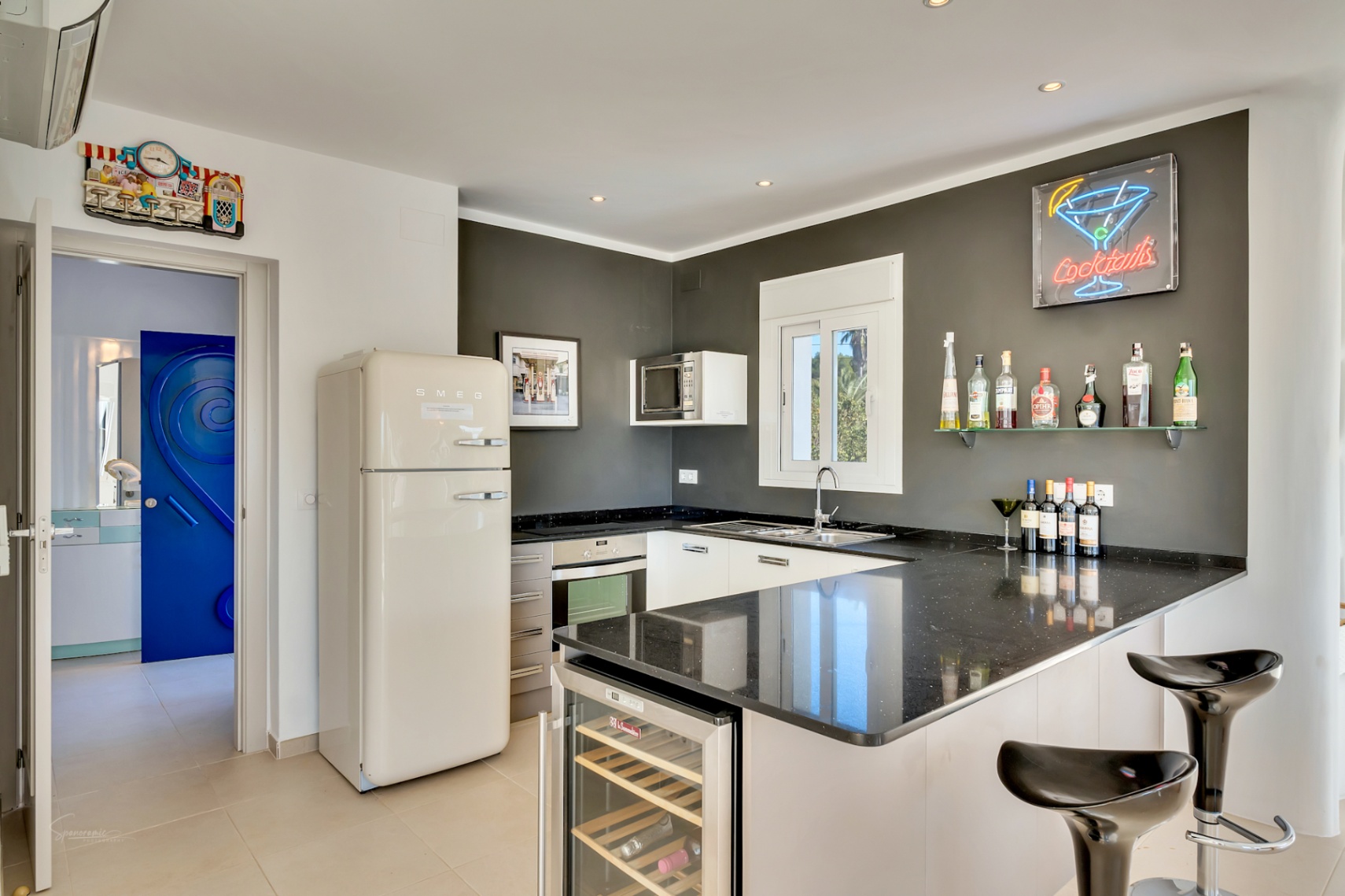 Moderne Küche mit schwarzen Granitarbeitsplatten, Smeg-Kühlschrank im Retro-Stil und Barbereich mit integriertem Weinkühlschrank und Neon-Akzenten.