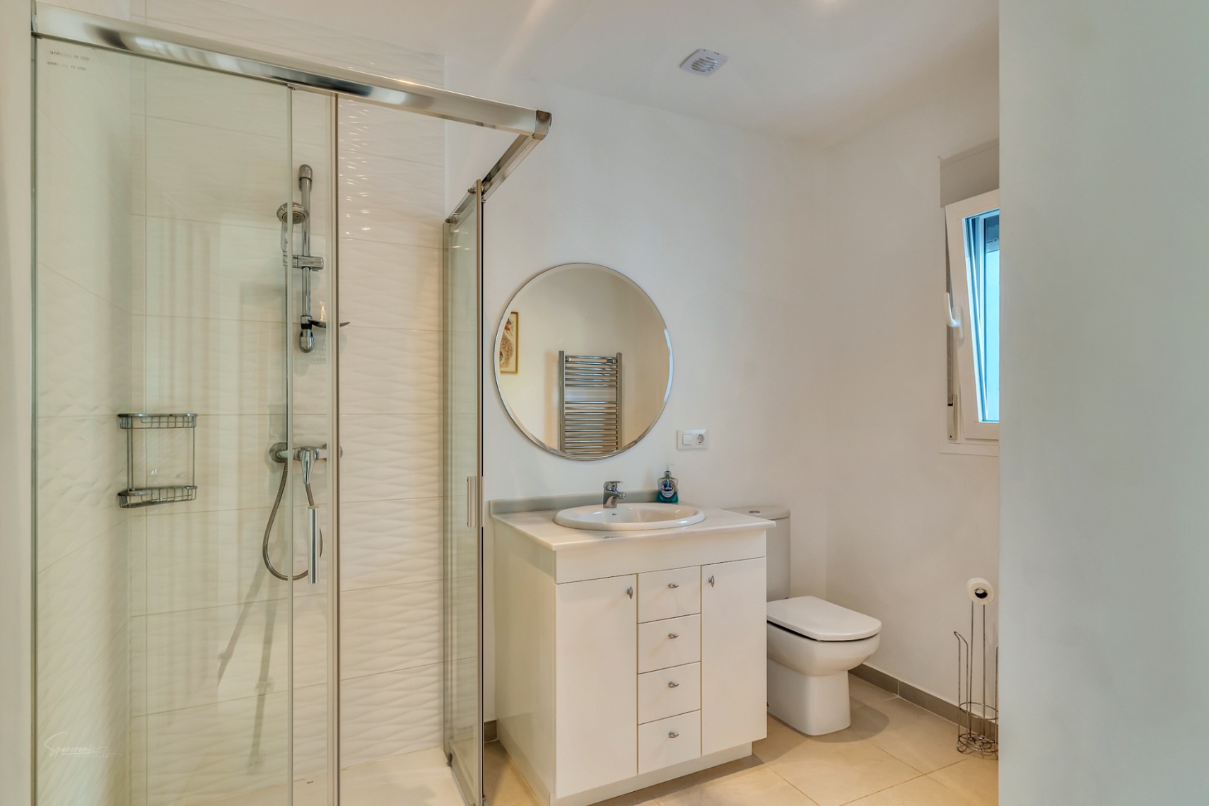 Modernes Badezimmer mit Glasduschkabine, strukturierten weißen Fliesen, weißem Waschtisch mit Rundspiegel und Tageslicht durch ein Seitenfenster.