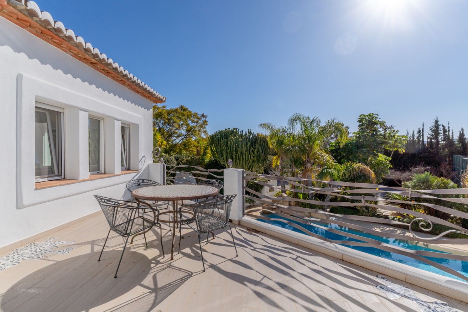 Obere Terrasse mit Mosaiktisch, wellenförmigem Metallgeländer und hellem Fliesenboden, mit Blick auf den privaten Pool und den mediterranen Garten mit Palmen.
