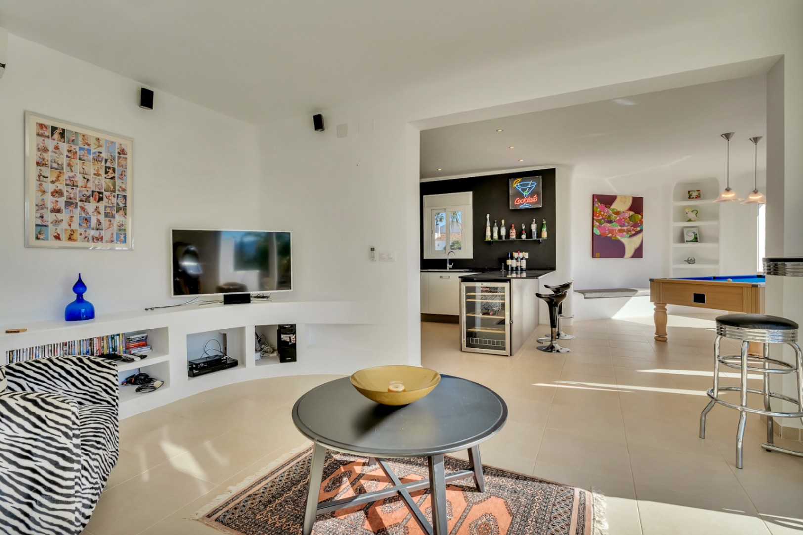 Offener Wohnbereich mit geschwungenem TV-Einbauregal, einem Billardtisch und einer Bar mit integriertem Weinkühlschrank und modernem Design.