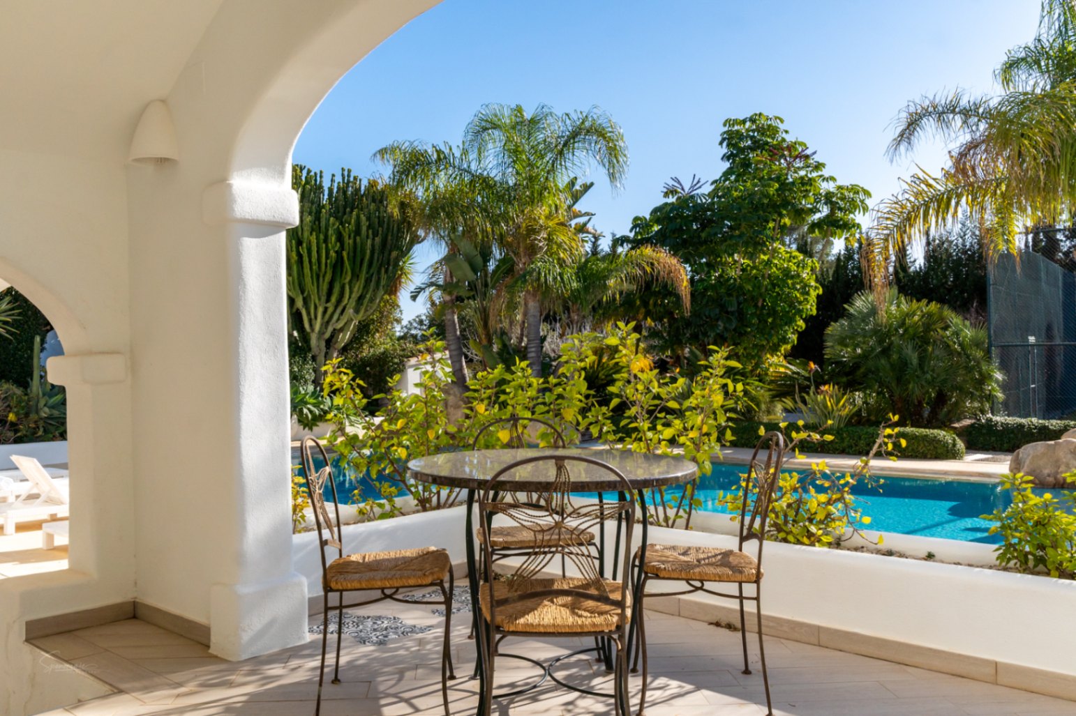 Überdachte Naya im Ibiza-Stil mit weißen Rundbögen, ausgestattet mit Schmiedeeisen-Möbeln und Blick auf den privaten Pool und den mediterranen Garten.