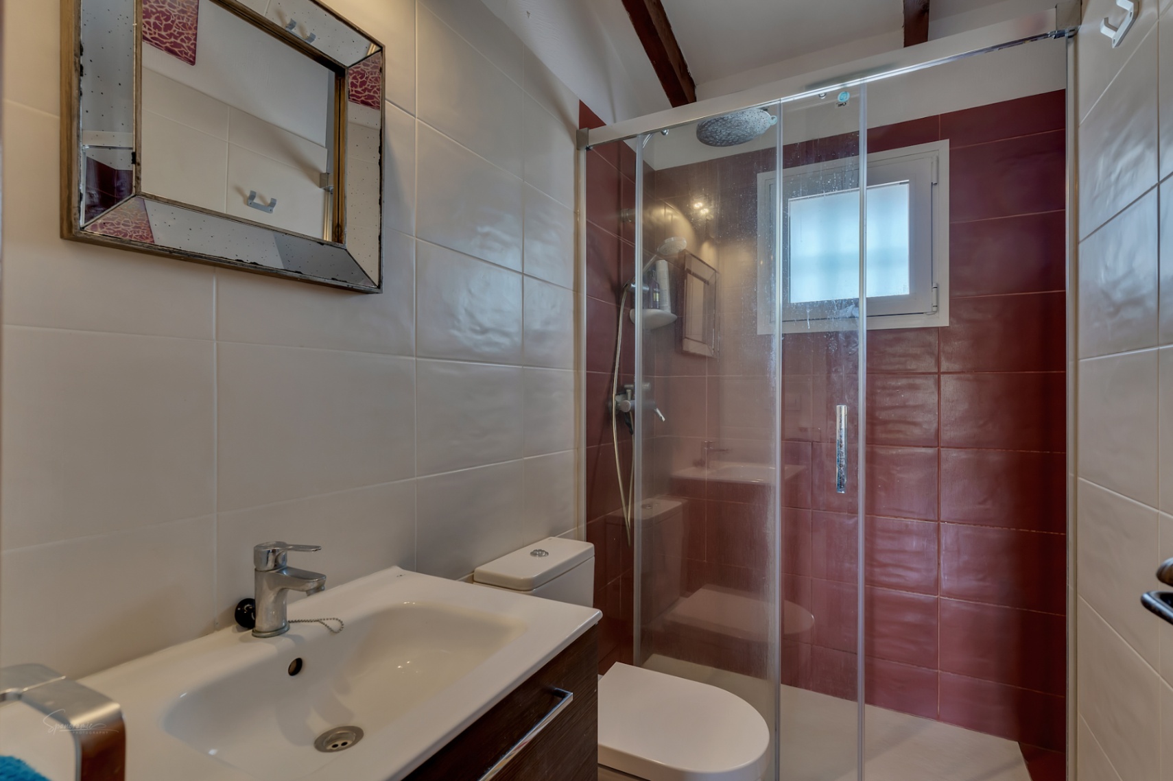 Badezimmerdetail mit Glasdusche, modernem Waschbecken und Fliesen in neutralen und burgunderfarbenen Tönen.