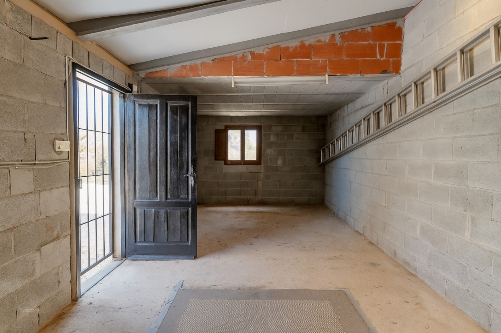 Garage mit Betonblockwänden, offener Holztür und Metallleiter.