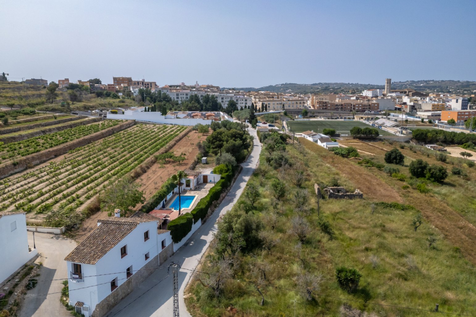 Luftaufnahme eines Landhauses mit Pool in Teulada, umgeben von Weinbergen und mediterraner Vegetation.