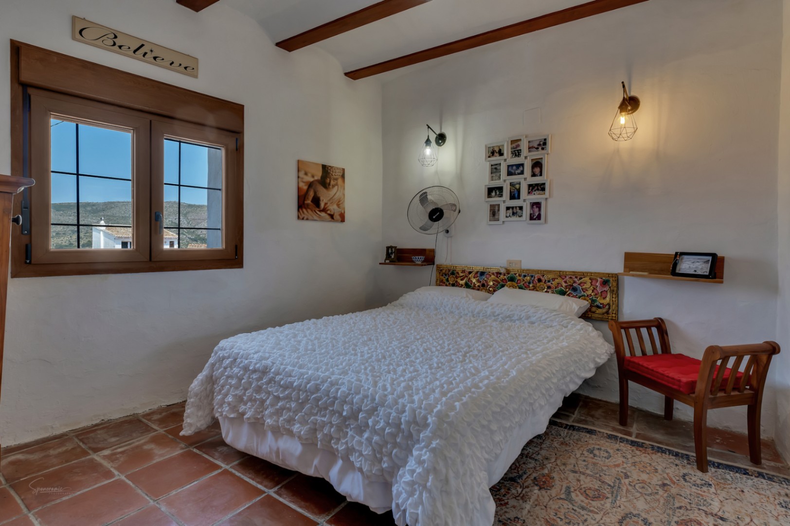 Rustikales Schlafzimmer mit Terrakottaboden, Doppelbett mit geschnitztem Kopfteil und Fenster mit Außenansicht.
