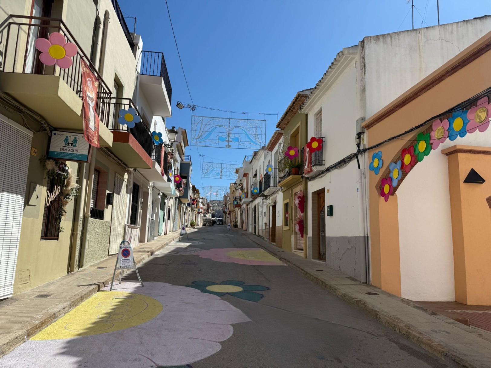 Straße in Teulada, geschmückt mit gemalten Blumen und hängenden Festtagsornamenten.