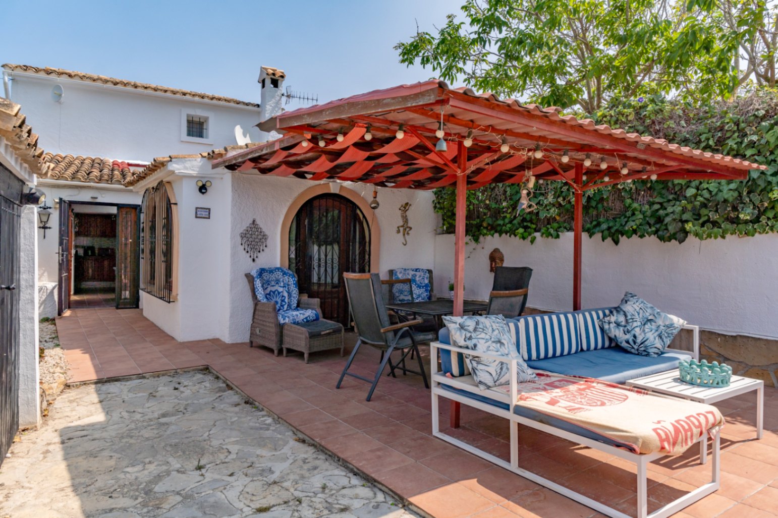 Überdachte Terrasse mit roter Markise, Gartenmöbeln und Zugang zum Landhaus in Teulada.