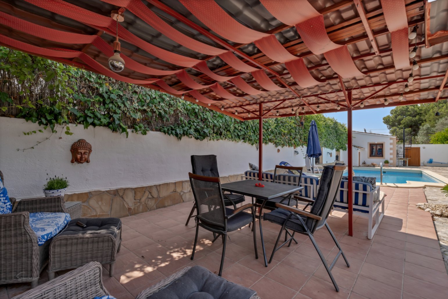 Überdachte Terrasse mit roter Markise und Fliesenboden. Weiße Wand mit Buddha-Dekor und vertikalem Garten.
