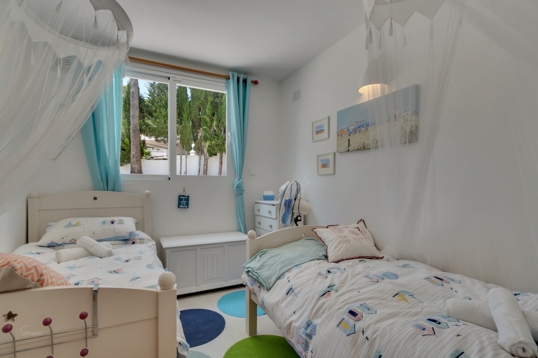 Helles Kinderzimmer mit zwei Einzelbetten, Dekoration im Strandstil und Blick nach draußen.