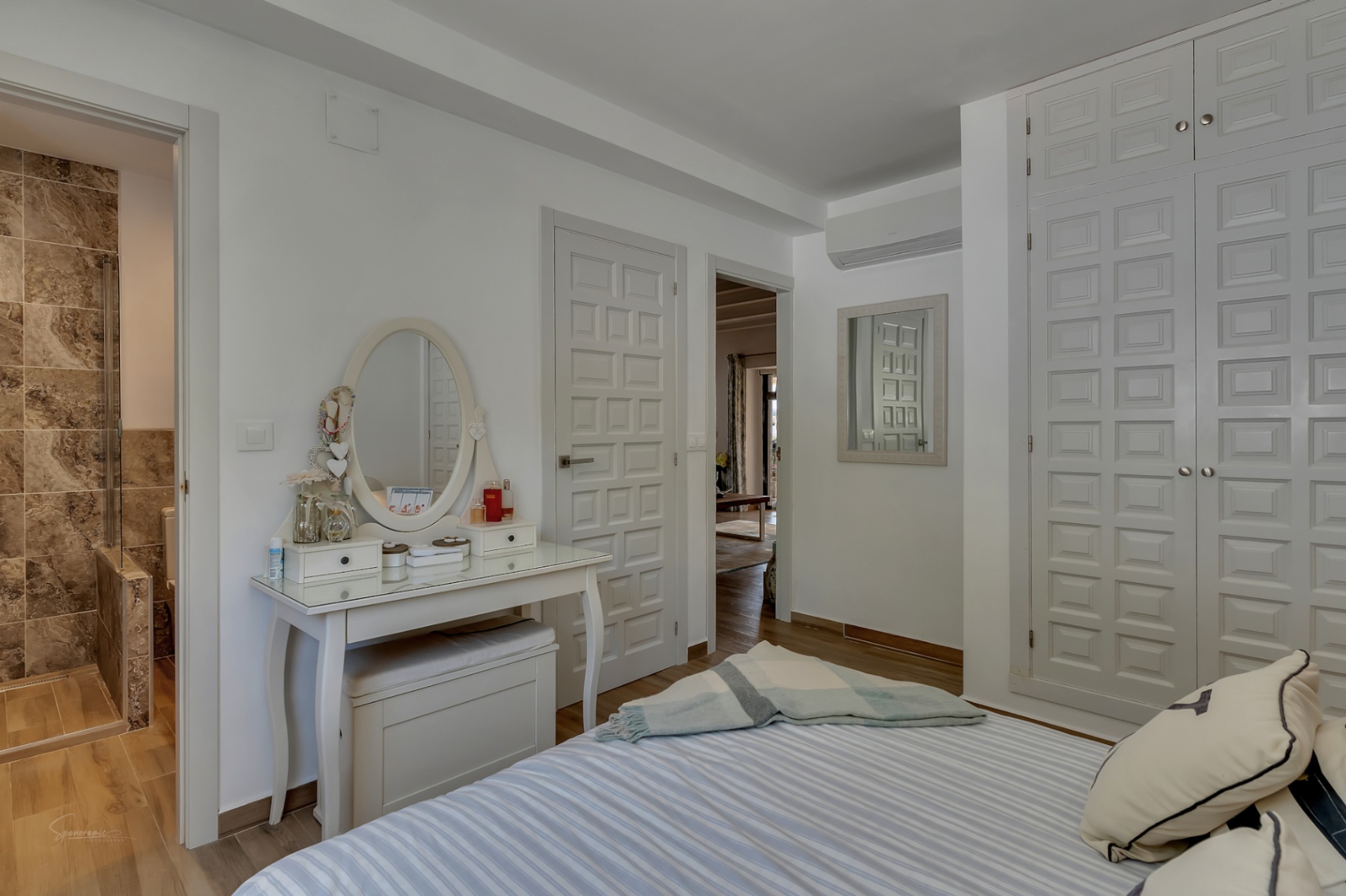 Helles Schlafzimmer mit weißem Schminktisch, Einbauschrank und Bad en Suite mit Steinfliesen.