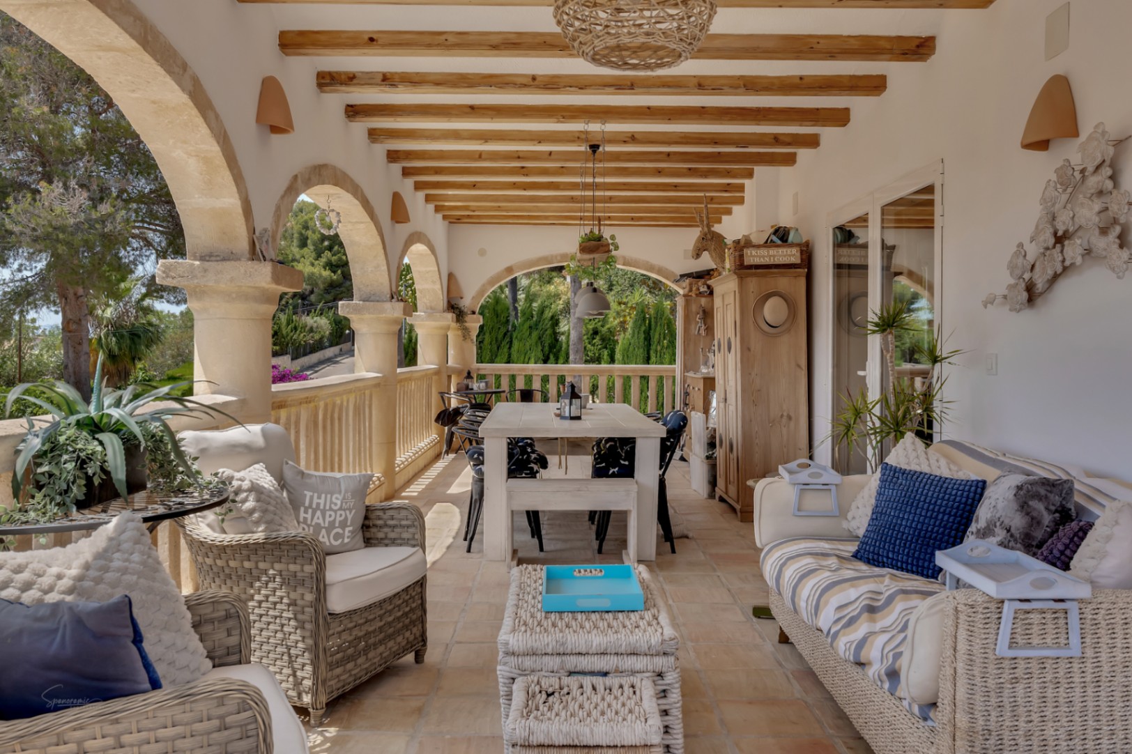 Veranda mit Steinbögen, Holzbalken und Rattanmöbeln, die einen hellen und einladenden Außenbereich schaffen.