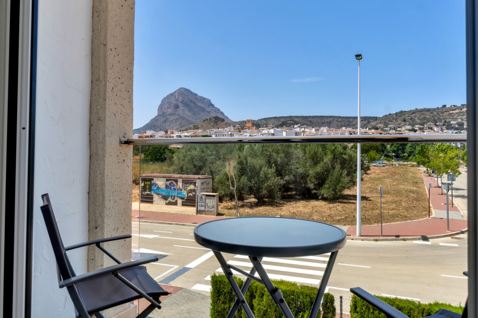 Balkon mit Glasgeländer und Sitzgelegenheit, der einen weiten Blick auf den Berg Montgó und die Altstadt von Jávea bietet.
