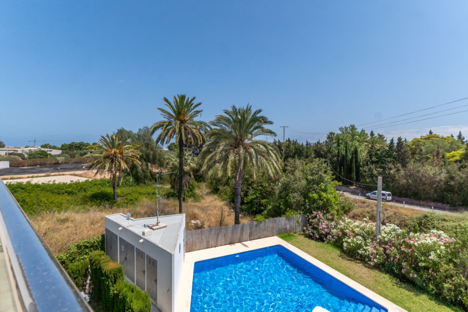 Blick von der oberen Terrasse auf den Gemeinschaftspool, die gepflegte Gartenanlage mit Palmen und die weite, sonnige Umgebung.