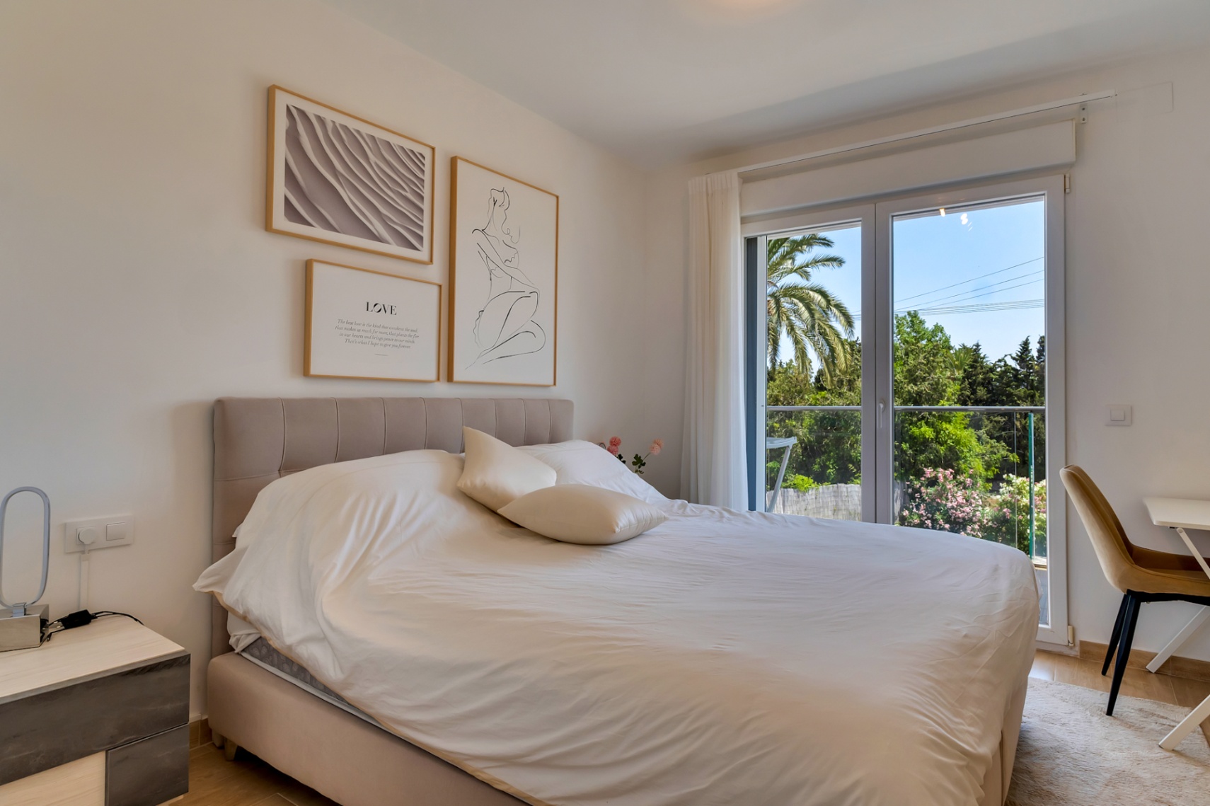 Doppelzimmer mit gepolstertem Kopfteil, Arbeitsbereich und Zugang zu einem Balkon mit Blick auf die mediterrane Bepflanzung.