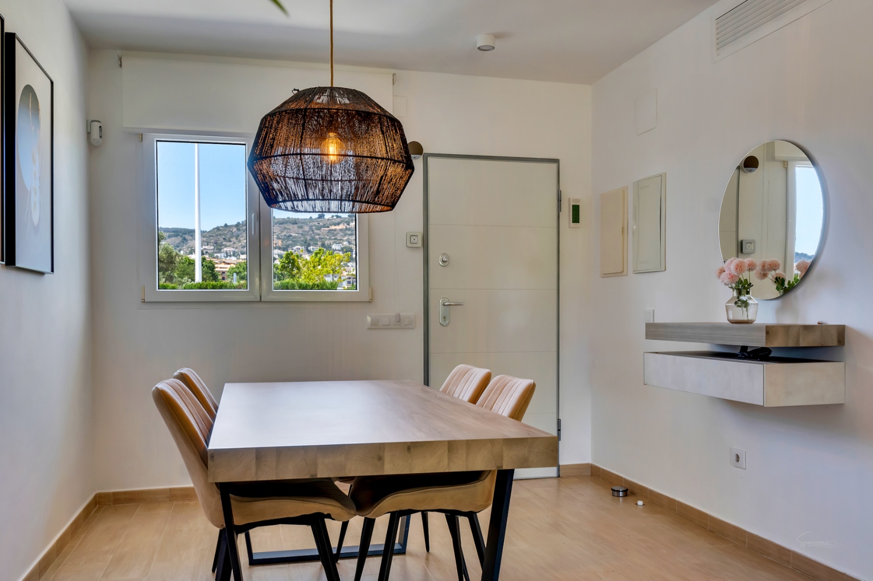 Essbereich mit massivem Holztisch, Polsterstühlen und einer dekorativen Korbgeflecht-Leuchte. Ein schwebendes Sideboard mit Rundspiegel akzentuiert den hellen Raum mit Ausblick.