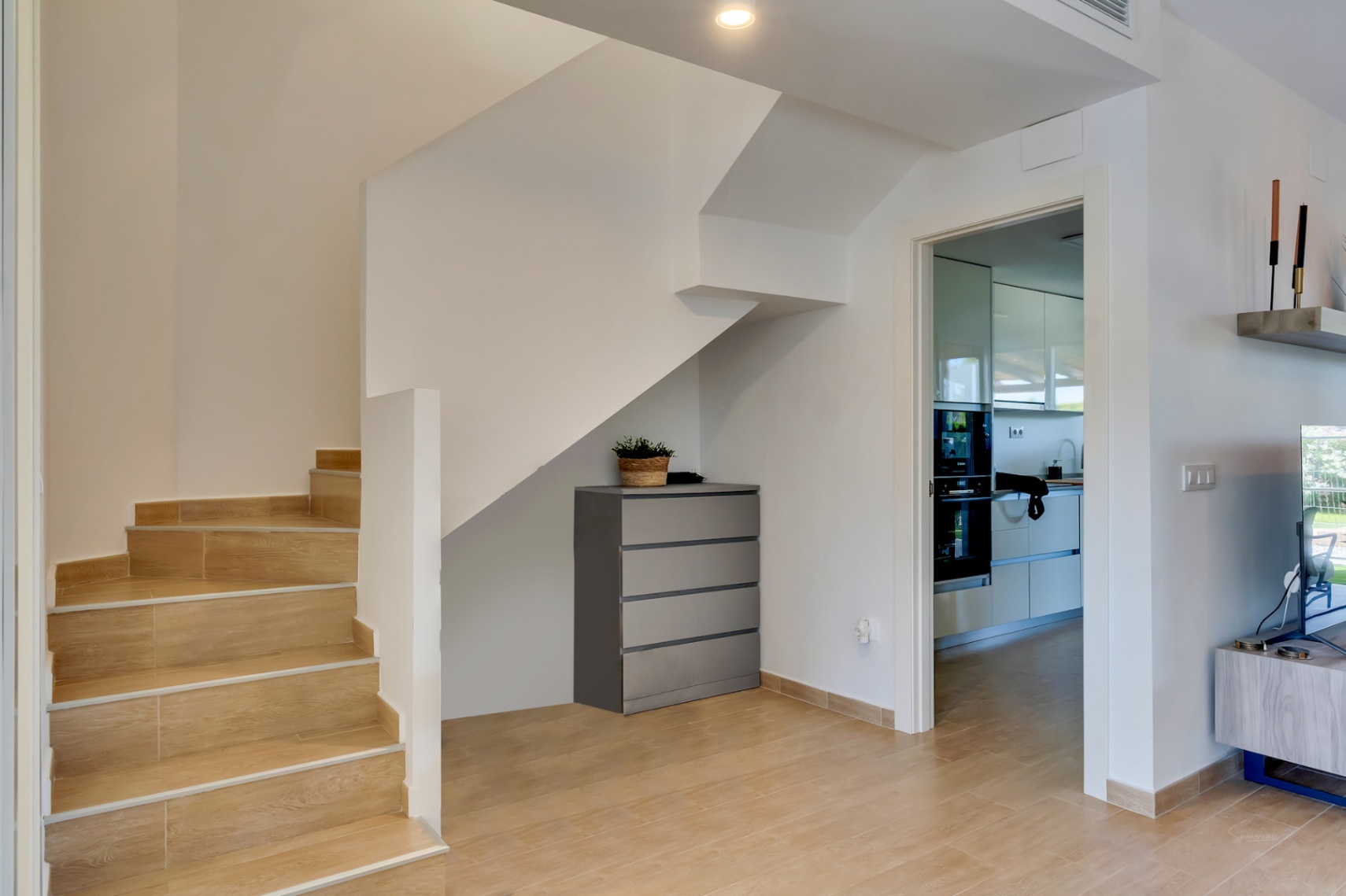 Flurbereich mit Treppe in Holzoptik-Fliesen, Stauraum unter der Treppe und Blick in die moderne, voll ausgestattete Einbauküche.
