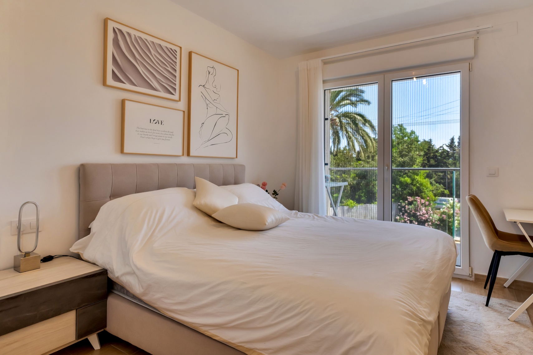 Helles Schlafzimmer mit Doppelbett, gepolstertem Kopfteil und Arbeitsbereich. Große Glastüren mit Fliegengittern führen auf einen privaten Balkon mit Blick ins Grüne.