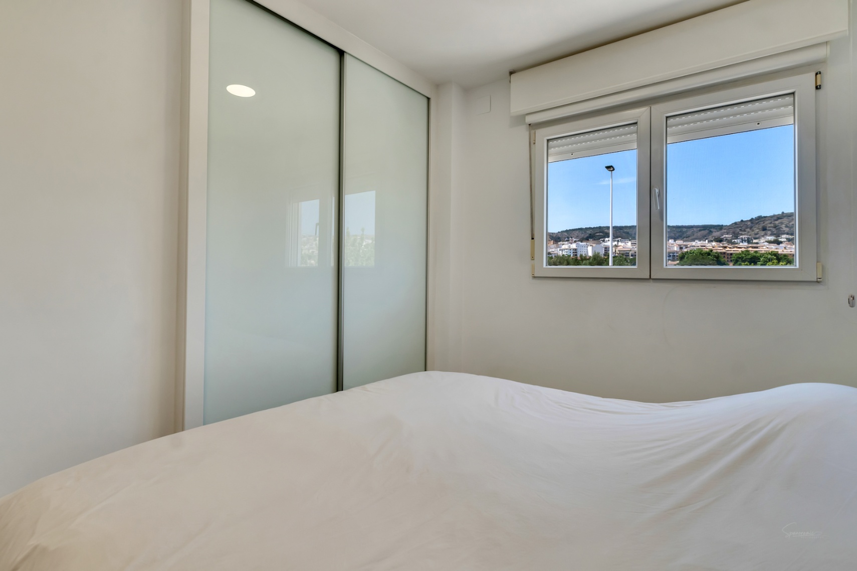Helles Schlafzimmer mit Einbauschrank mit Schiebetüren aus Milchglas und doppelt verglastem Fenster mit Blick auf die umliegende Landschaft.