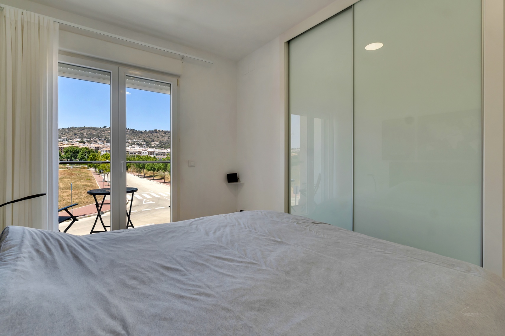 Helles Schlafzimmer mit großem Einbauschrank mit Glasschiebetüren und Zugang zu einem privaten Balkon mit Blick auf die umliegende Landschaft.