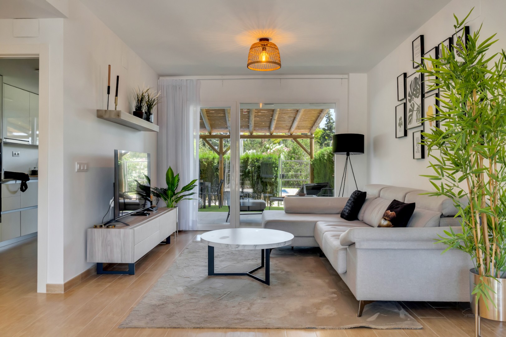 Helles Wohnzimmer mit L-Sofa, Marmortisch und großen Glasschiebetüren, die direkt auf die private Terrasse mit Holzpergola und Blick ins Grüne führen.