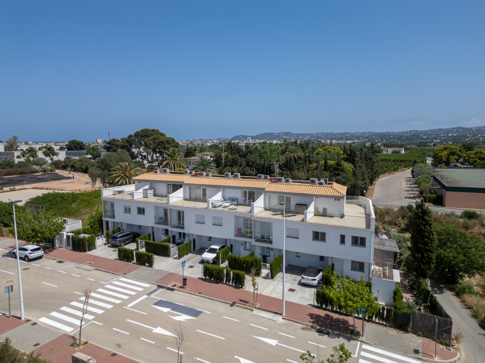 Luftaufnahme der modernen Reihenhausanlage mit privaten Parkplätzen vor dem Haus, weißen Fassaden und großzügigen Terrassen mit Glasgeländern auf mehreren Ebenen.