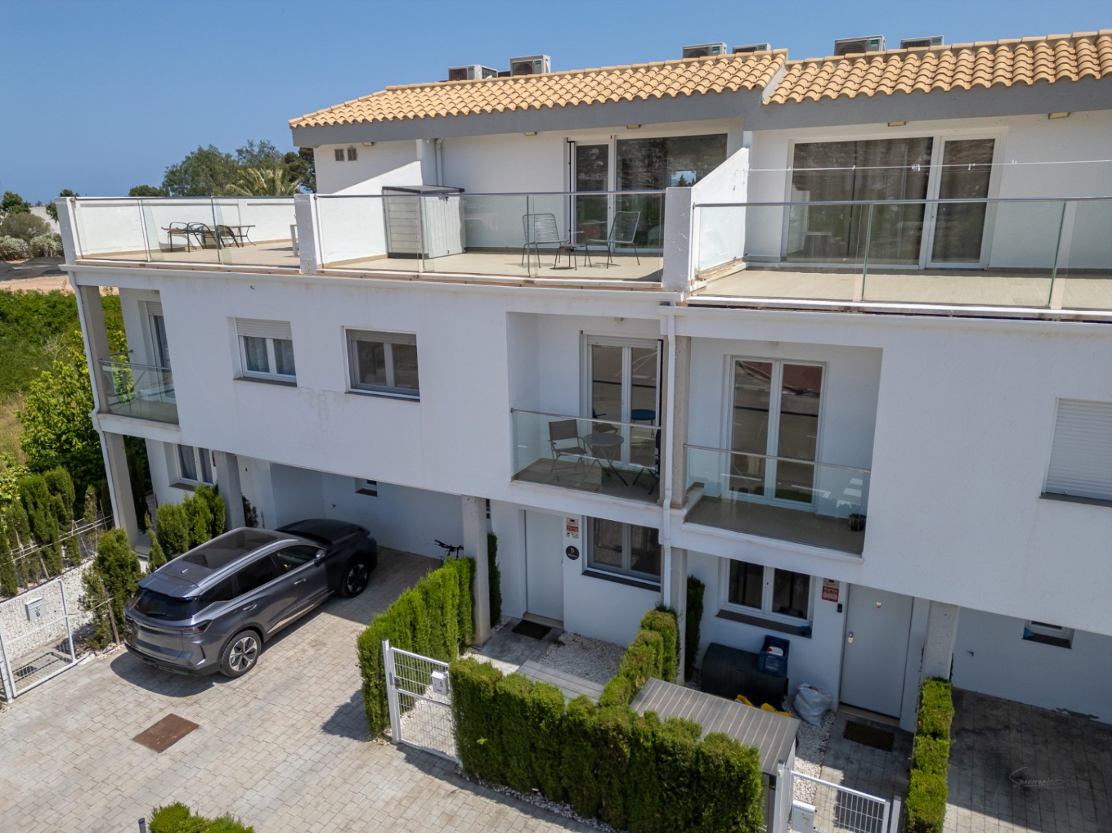 Moderne dreistöckige Fassade mit großzügigen Dachterrassen, Glasgeländern und privaten Parkplätzen direkt vor dem Eingang.