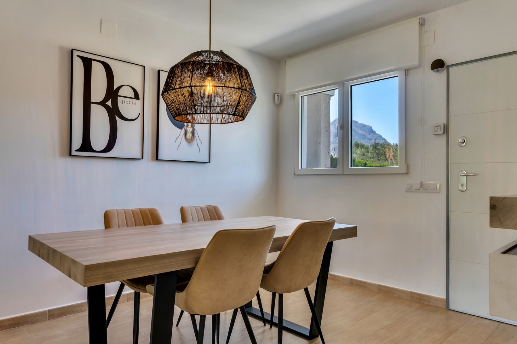 Moderner Essbereich mit Holztisch, Polsterstühlen und einer Hängeleuchte aus Geflecht. Das Fenster bietet einen Blick auf das Montgó-Massiv.