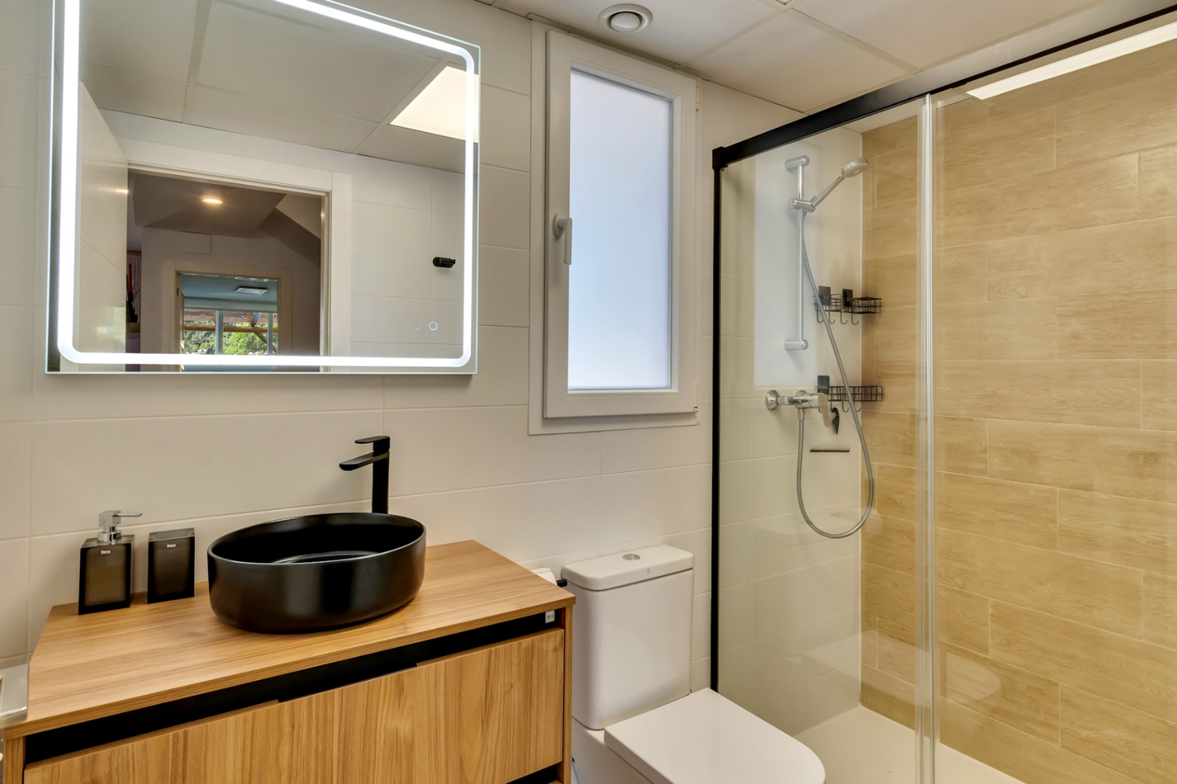 Modernes Badezimmer mit schwarzem Aufsatzwaschbecken auf Holzmöbel, LED-Spiegel und begehbarer Dusche mit schwarzen Profilen und Fliesen in Holzoptik.