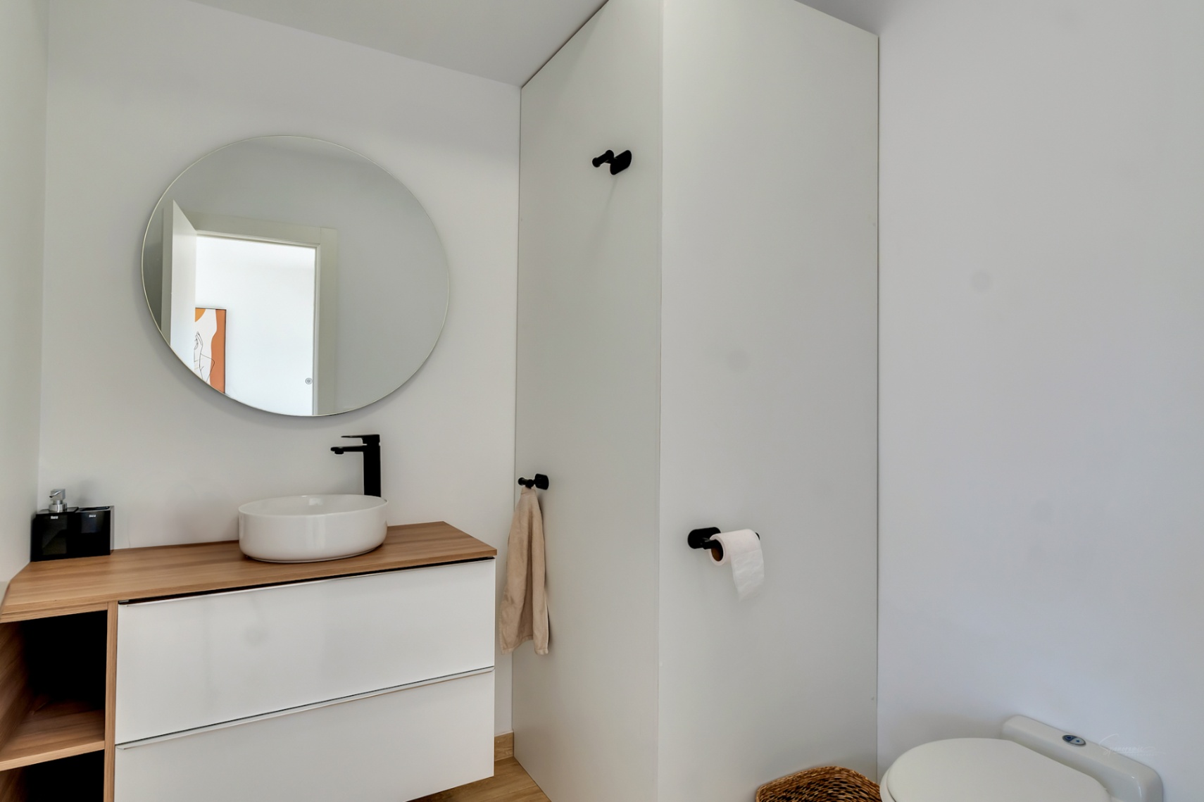 Modernes Gäste-WC mit Aufsatzwaschbecken auf einer Holzplatte, mattschwarzen Armaturen und einem runden Spiegel. Der weiße Hängeschrank sorgt für ein minimalistisches Design.