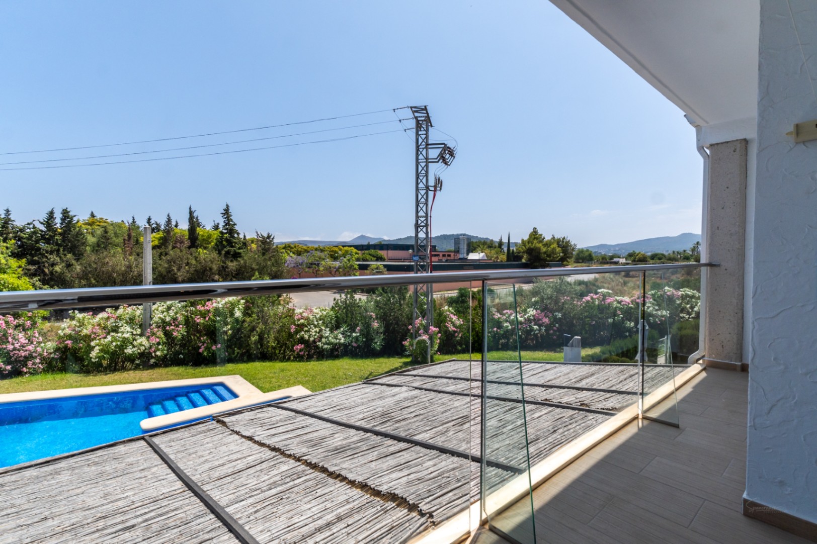 Obere Terrasse mit Glas- und Edelstahlgeländer, Blick auf den Gemeinschaftspool und die private Terrasse mit einer natürlichen Schilfrohr-Pergola.
