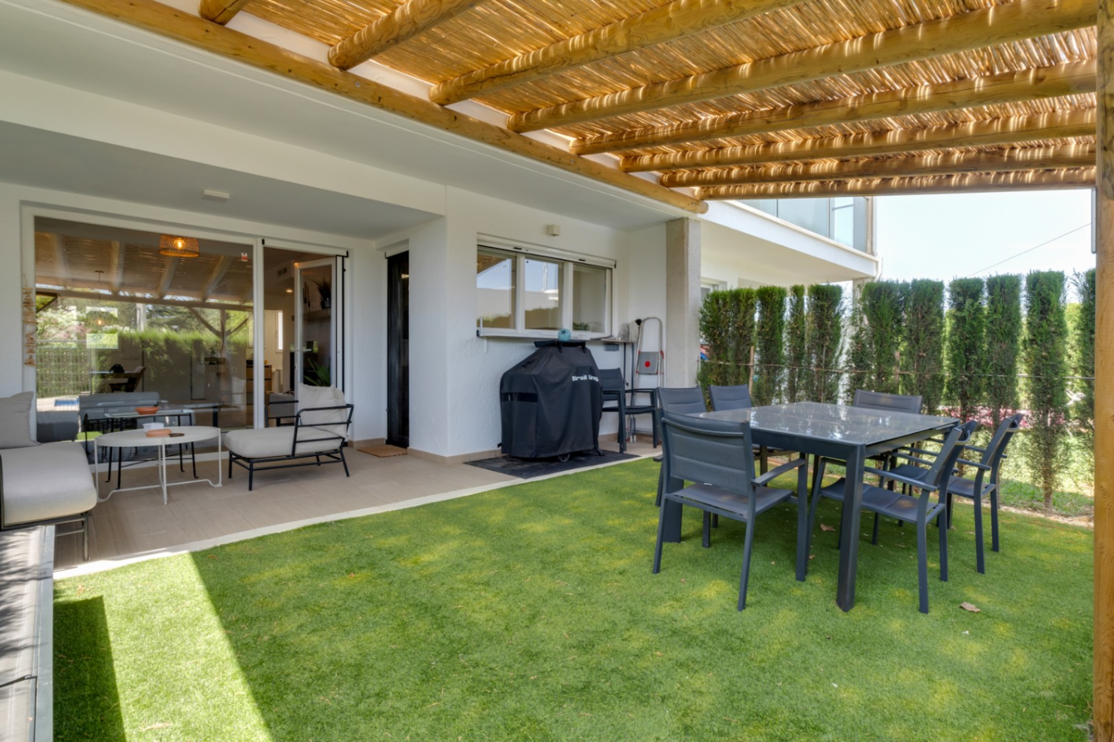 Private Terrasse mit Kunstrasen, Holzpergola und Essbereich im Freien. Verfügt über eine Lounge-Ecke und Grill, mit direktem Zugang zum Wohnbereich durch Glasschiebetüren.