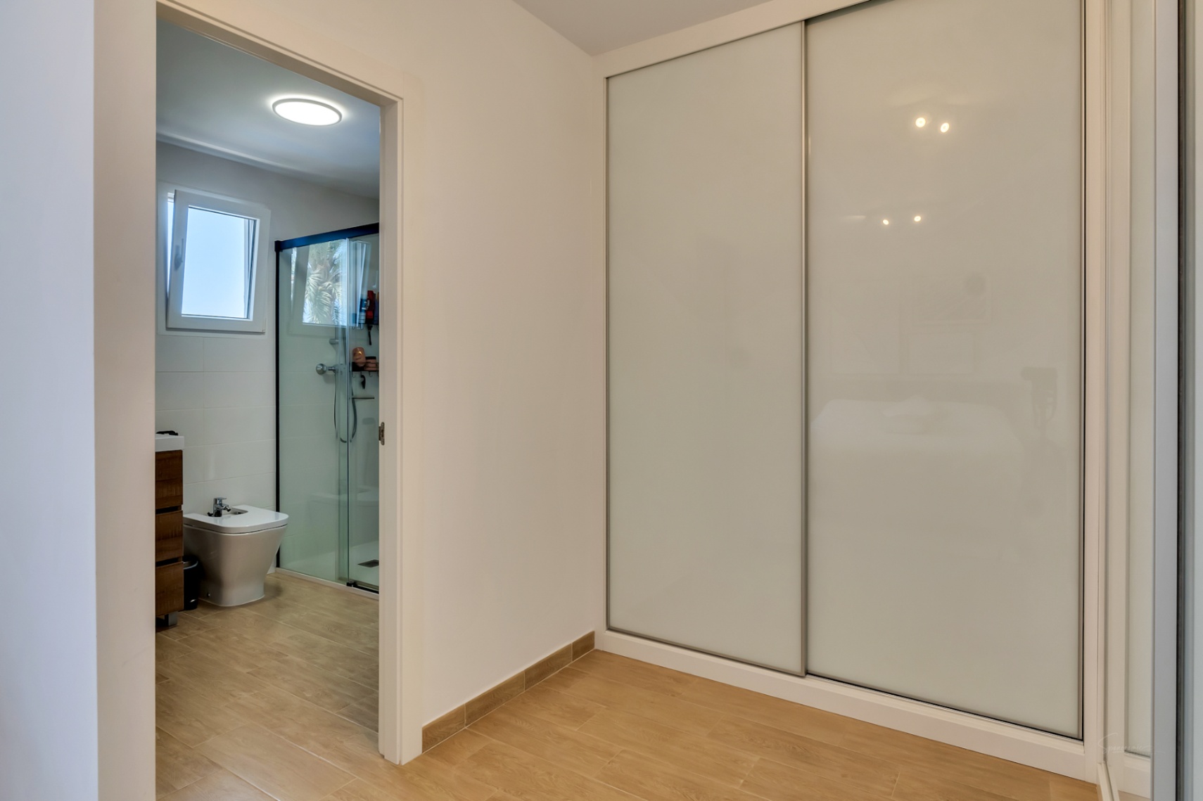 Schlafzimmer mit großem Einbauschrank mit weißen Schiebetüren und direktem Zugang zum modernen En-Suite-Badezimmer mit ebenerdiger Dusche.