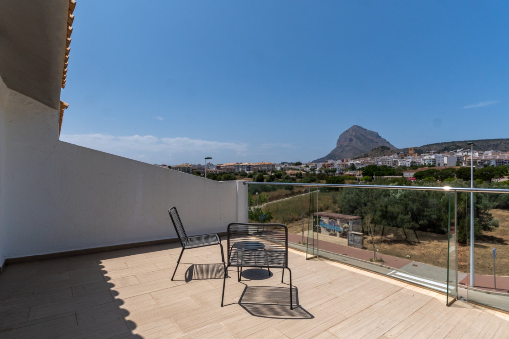 Terrasse im Obergeschoss mit Glasgeländer und Panoramablick auf den Montgó und Jávea. Ausgestattet mit minimalistischen schwarzen Außenmöbeln auf hellem Fliesenboden.