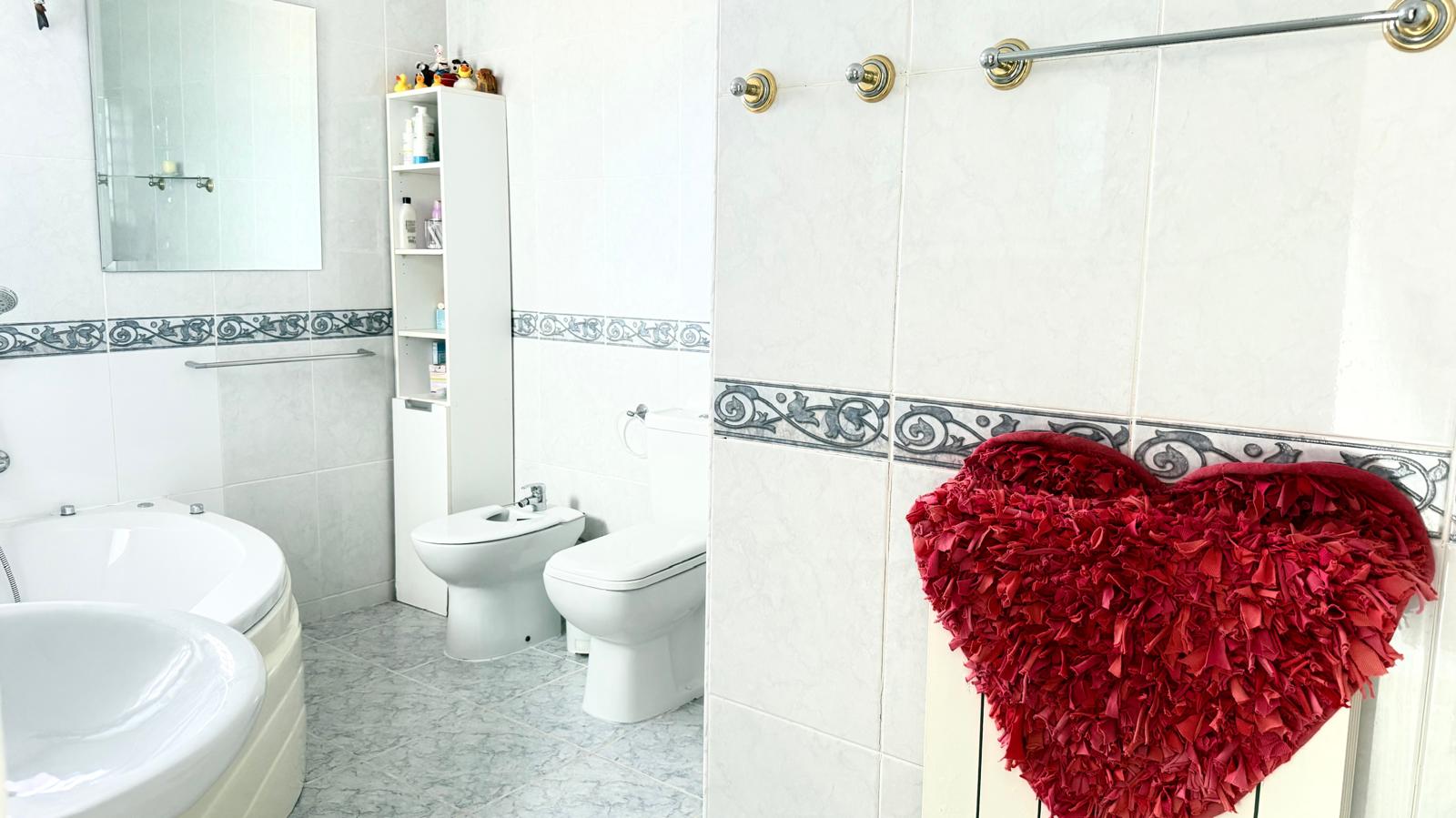 Badezimmer mit Eck-Whirlpool-Badewanne, Bidet und WC, gestaltet mit weißen Wandfliesen, einer Zierbordüre und goldfarbenen Details.