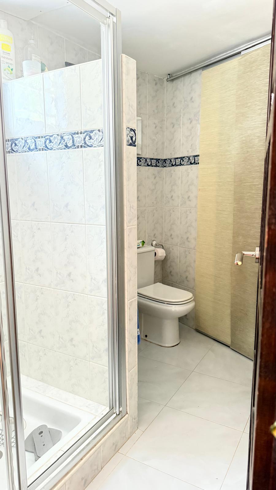 Badezimmer mit Glasduschkabine, marmorierten Wandfliesen mit blauer Zierbordüre und weißen Sanitärobjekten sowie einer platzsparenden Schiebetür.