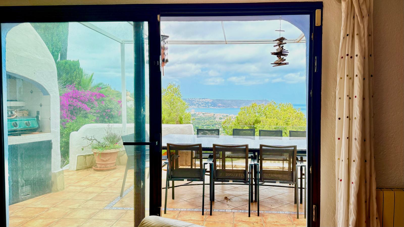 Blick von innen auf die Hauptterrasse mit Essbereich im Freien, gemauertem Grill und Panoramablick über die Bucht von Jávea bis hin zum Mittelmeer.